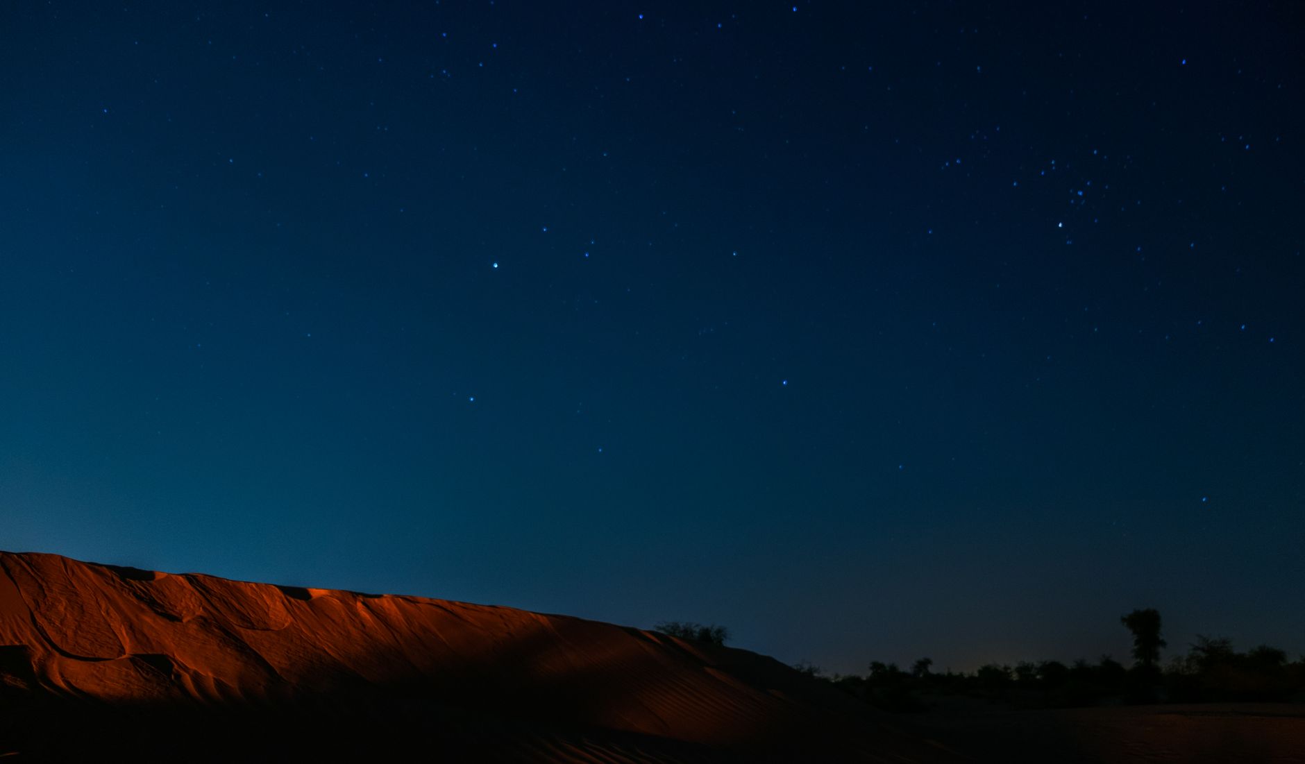 Expansive starry sky over terracotta desert sand dunes